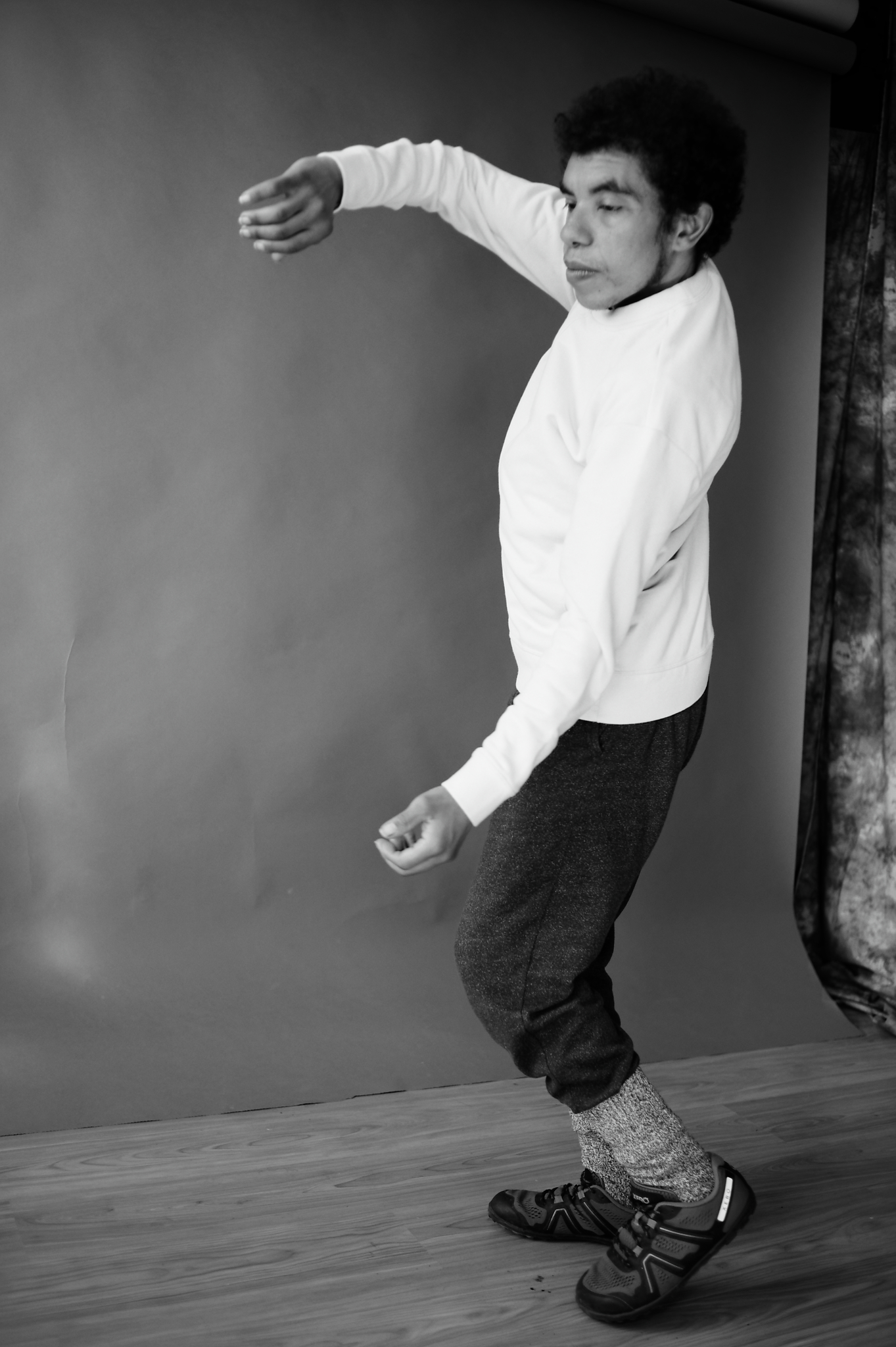 Full body black and white photo of DJ from the side dancing, he is using his arms to turn